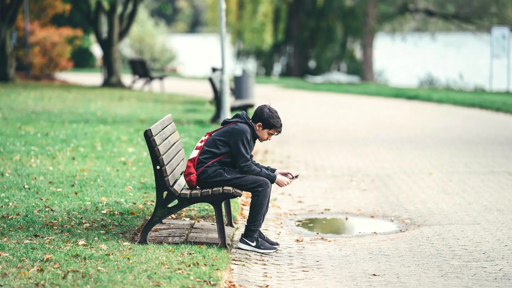 Teen boy sits alone on a park bench while viewing his mobile
